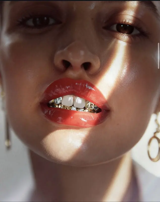 A close up of a woman showing off her teeth which are gold and silver